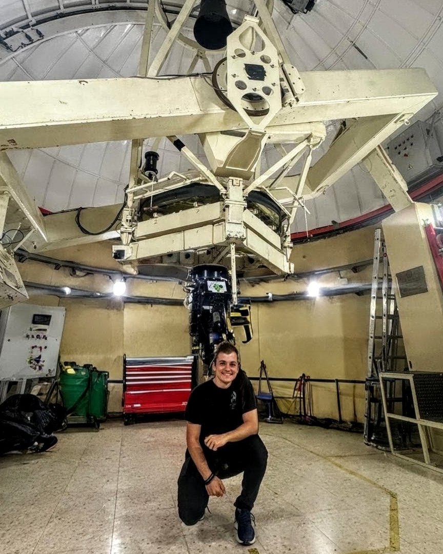Andrés Vicente Arévalo kneeling beneath a telescope inside an observatory dome